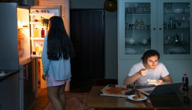 Pessoa comendo de madrugada na cozinha iluminada pela geladeira