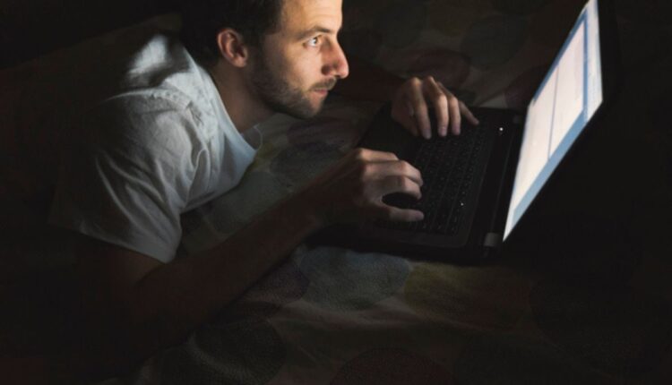 Homem usando notebook à noite em posição curvada